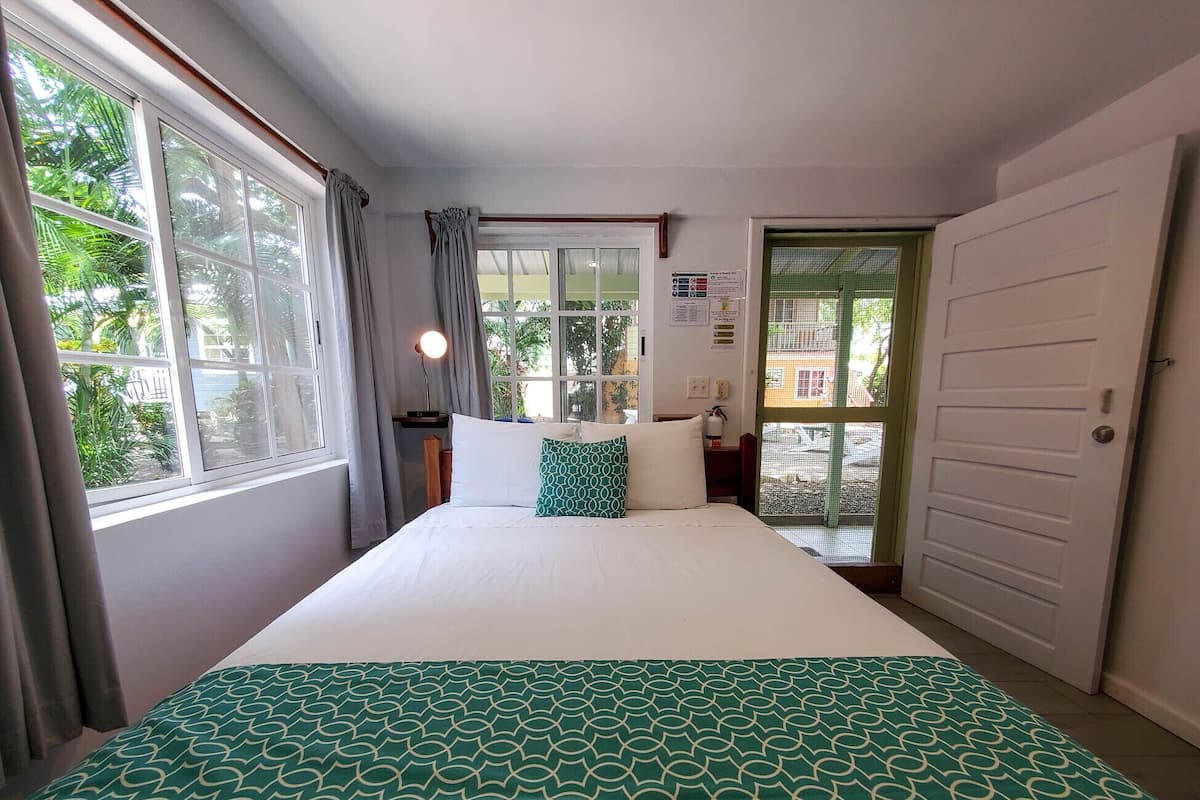A hotel room with a bed, a window with curtains, a door, and a wall with a bulletin board.