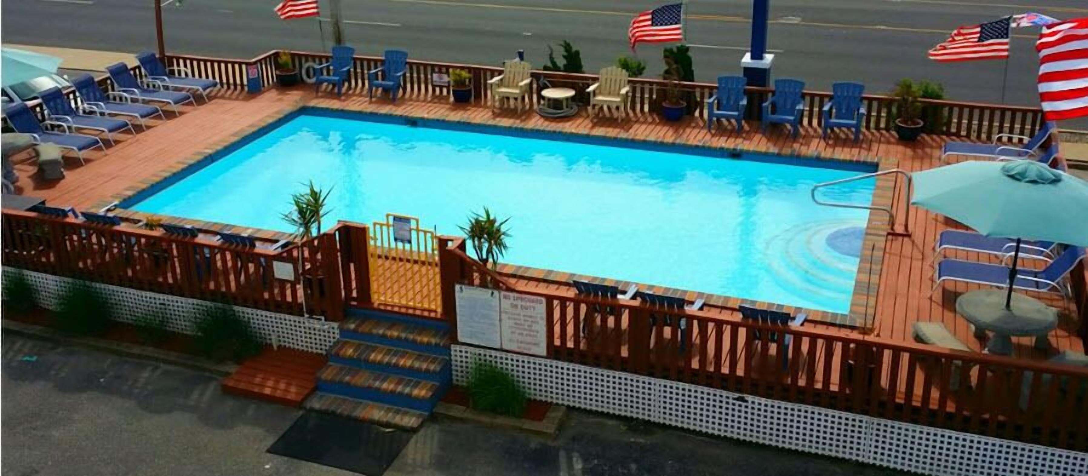 Ein rechteckiger Pool mit Holzterrasse und Liegestühlen. Amerikanische Flaggen und ein Schild, das einen privaten Bereich kennzeichnet.