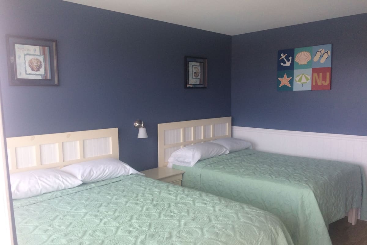 Une chambre avec deux lits, chacun doté d’une tête de lit et de linge de lit blanc. Des appliques murales et des œuvres d’art encadrées sont disposées au-dessus des lits.