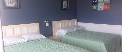 Habitación con dos camas, cada una con cabecera y ropa blanca. Hay luces fijadas a la pared y cuadros enmarcados sobre las camas.