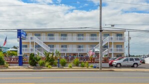 A two-story motel with a balcony on the second floor, a flag in front, and a parking lot with cars.