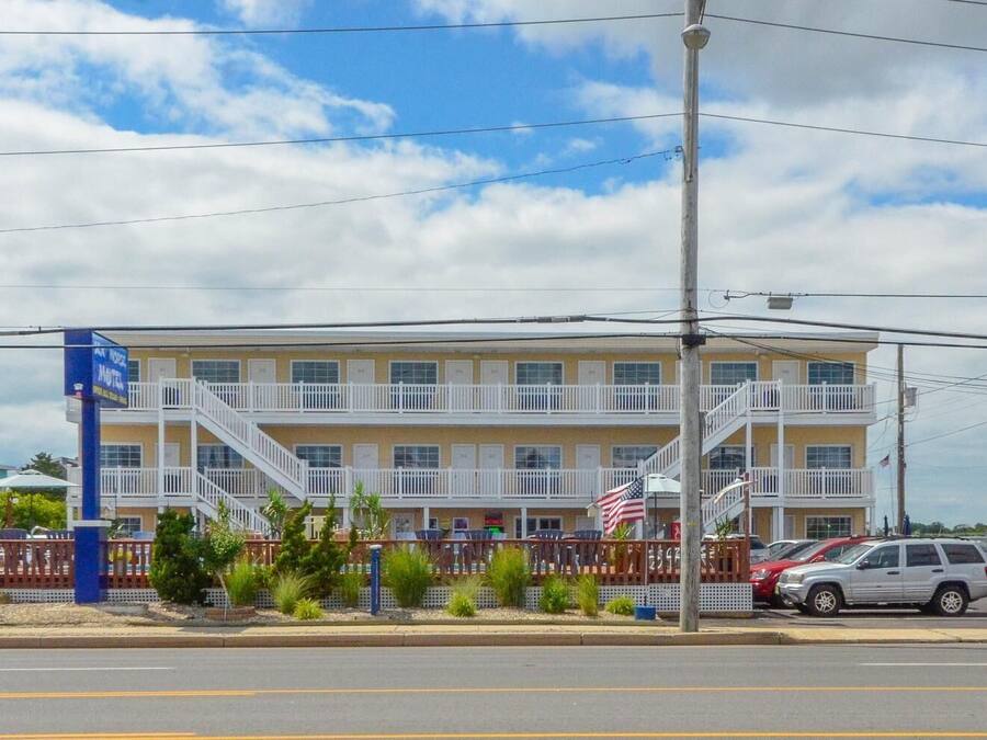 Un motel à deux étages, doté d’un balcon au deuxième étage, d’un drapeau devant l’entrée et d’un parking rempli de voitures.