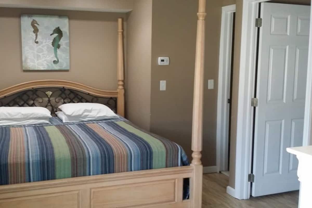 Un lit à baldaquin avec une couvre-lit à rayures, un tableau représentant un hippocampe accroché au mur et une porte blanche sur la droite.