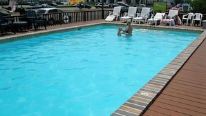 A swimming pool with a wooden deck and lounge chairs.