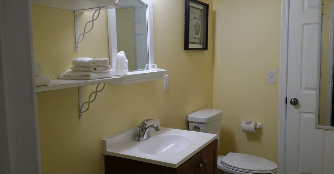 A bathroom with a white sink, a toilet, and a shelf with folded towels.