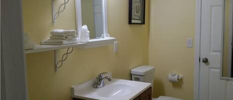 A bathroom with a white sink, a toilet, and a shelf with folded towels.