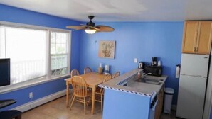 A compact kitchen with a dining table, chairs, a ceiling fan, a refrigerator, and a microwave.