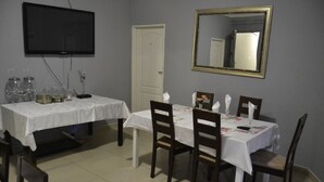 Un comedor con dos mesas, cada una con mantel blanco y sillas de madera. Un televisor de pantalla plana está montado en la pared sobre la mesa de la izquierda.