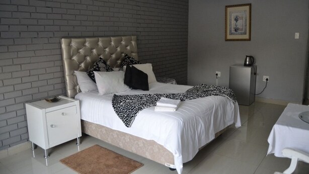 Un dormitorio con cabecera capitonada, una mesita de noche blanca, una cama con ropa de cama blanca y un plaid de leopardo, una pequeña mesa con una tetera, y un cuadro en la pared.