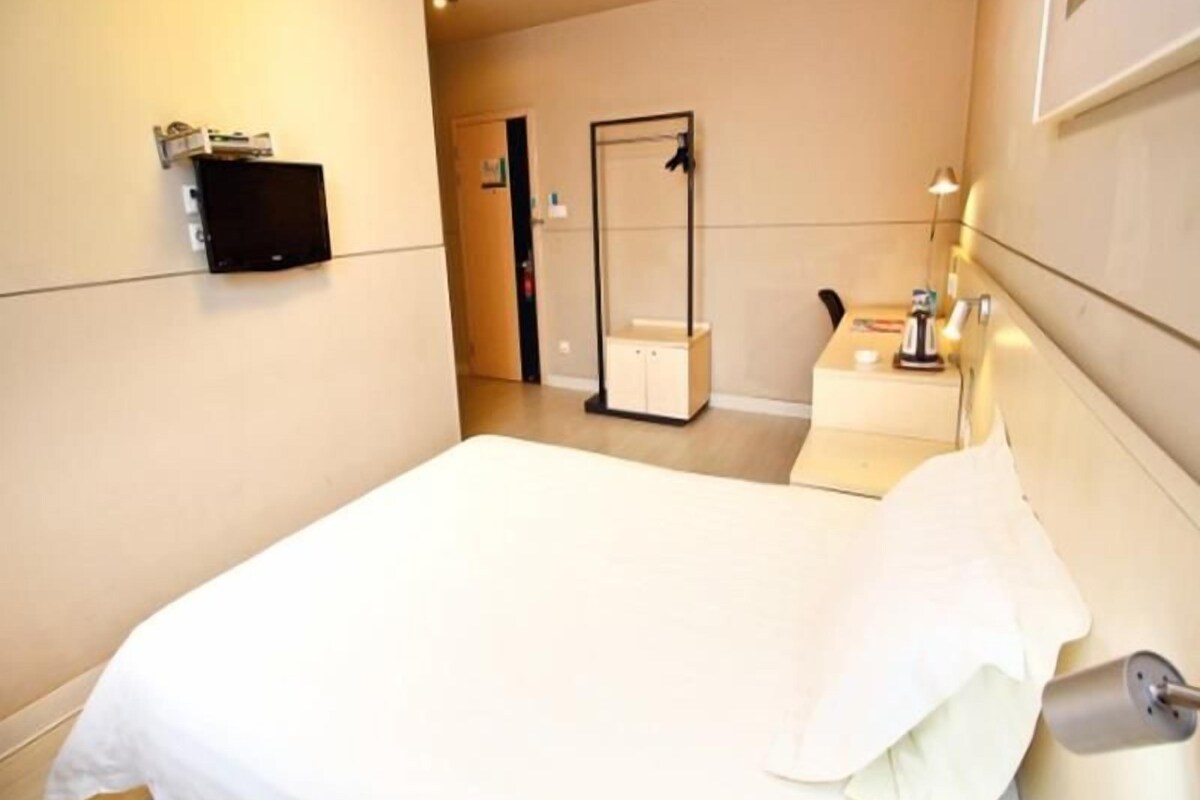 Een hotelkamer met een bed, nachtkastje, spiegel en een aan de muur bevestigde televisie.
