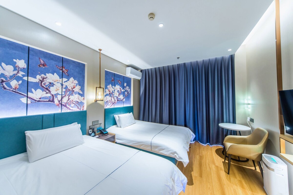 Een hotelkamer met twee bedden, een bureau, een stoel, een televisie en een schilderij aan de muur.