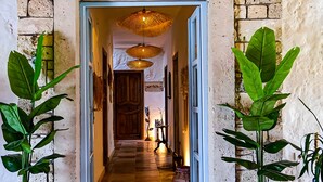 Um corredor com piso de madeira, uma porta branca no final e luminárias de vime penduradas.