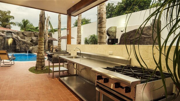 Zona junto a la piscina con barbacoa, mobiliario exterior y cocina equipada con estufa a gas.