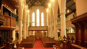 An interior of a church with wooden pews, a red carpet, and a high ceiling with arched windows. - TravelStop #London-Ealing (London)