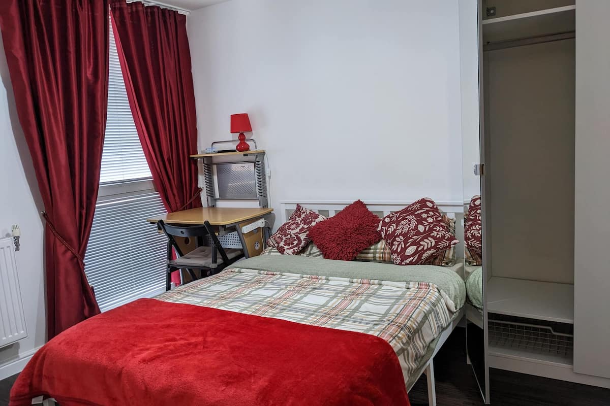 A bedroom with a bed, a desk, a chair, a wardrobe, and a radiator.