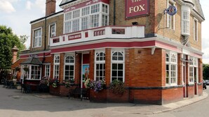 A traditional pub named "The Fox" with a red and white facade, multiple chimneys, and a signboard. - TravelStop #London-Ealing (London)