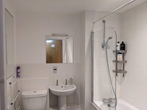A bathroom with a toilet, sink, and shower. There is a mirror above the sink and a showerhead above the bathtub. - TravelStop #London-Ealing (London)