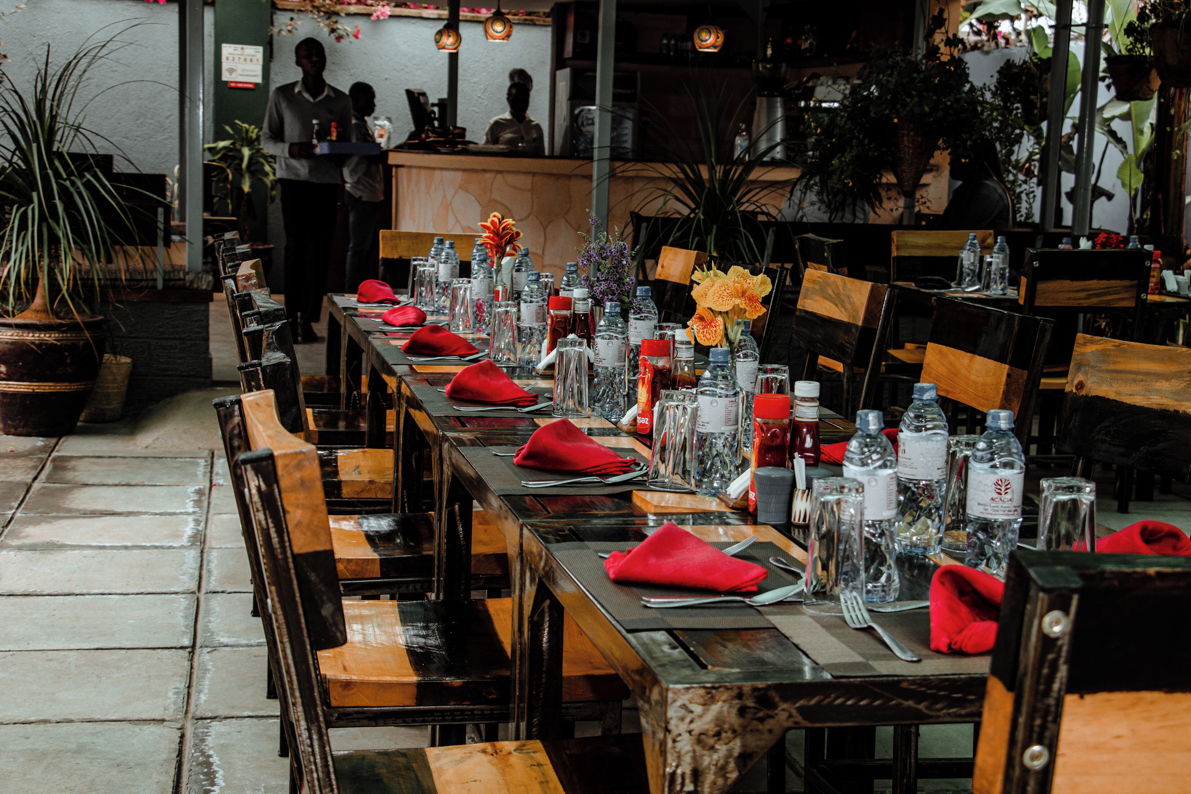 A restaurant with long wooden tables set for dining, each with red napkins, water bottles, and glassware.