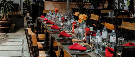 A restaurant with long wooden tables set for dining, each with red napkins, water bottles, and glassware.
