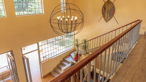 Una escalera con barandilla de madera, un candelabro y un escudo en la pared.