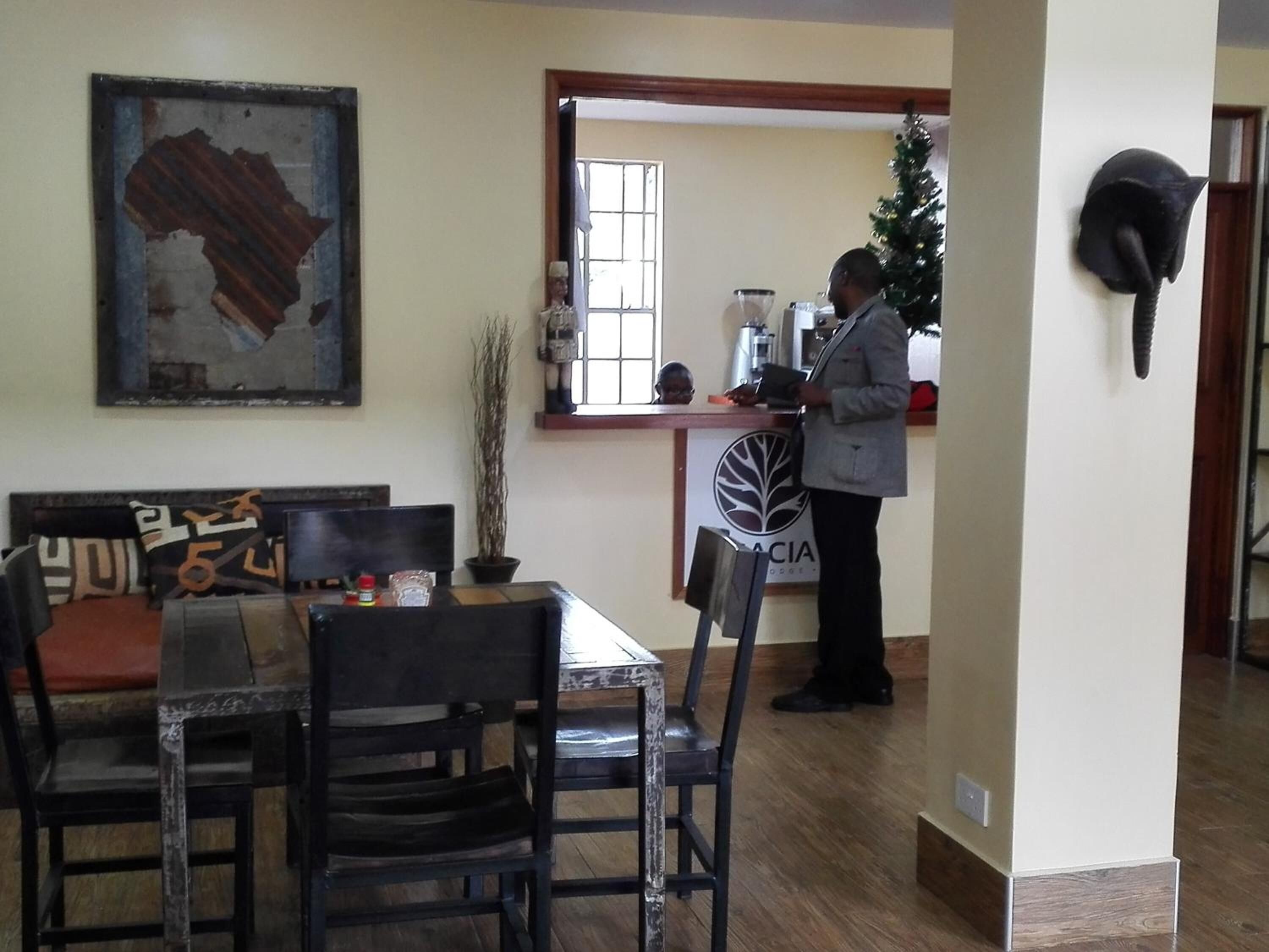 Un área de comedor con una mesa y sillas de madera, un tapiz decorativo y un mostrador de recepción con un árbol de Navidad.