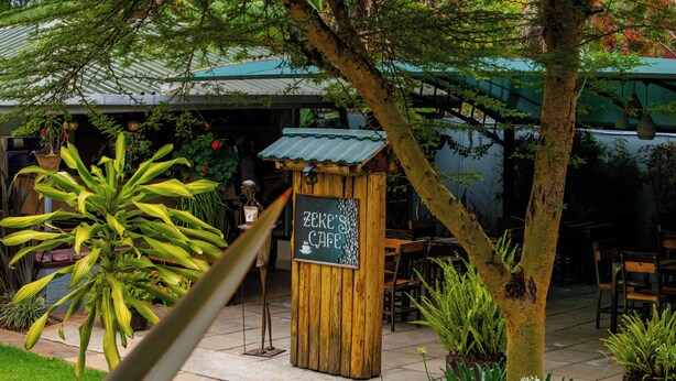 Un área de estar al aire libre con un letrero de madera que dice "ZERE'S CAFE" y diversas plantas y árboles.