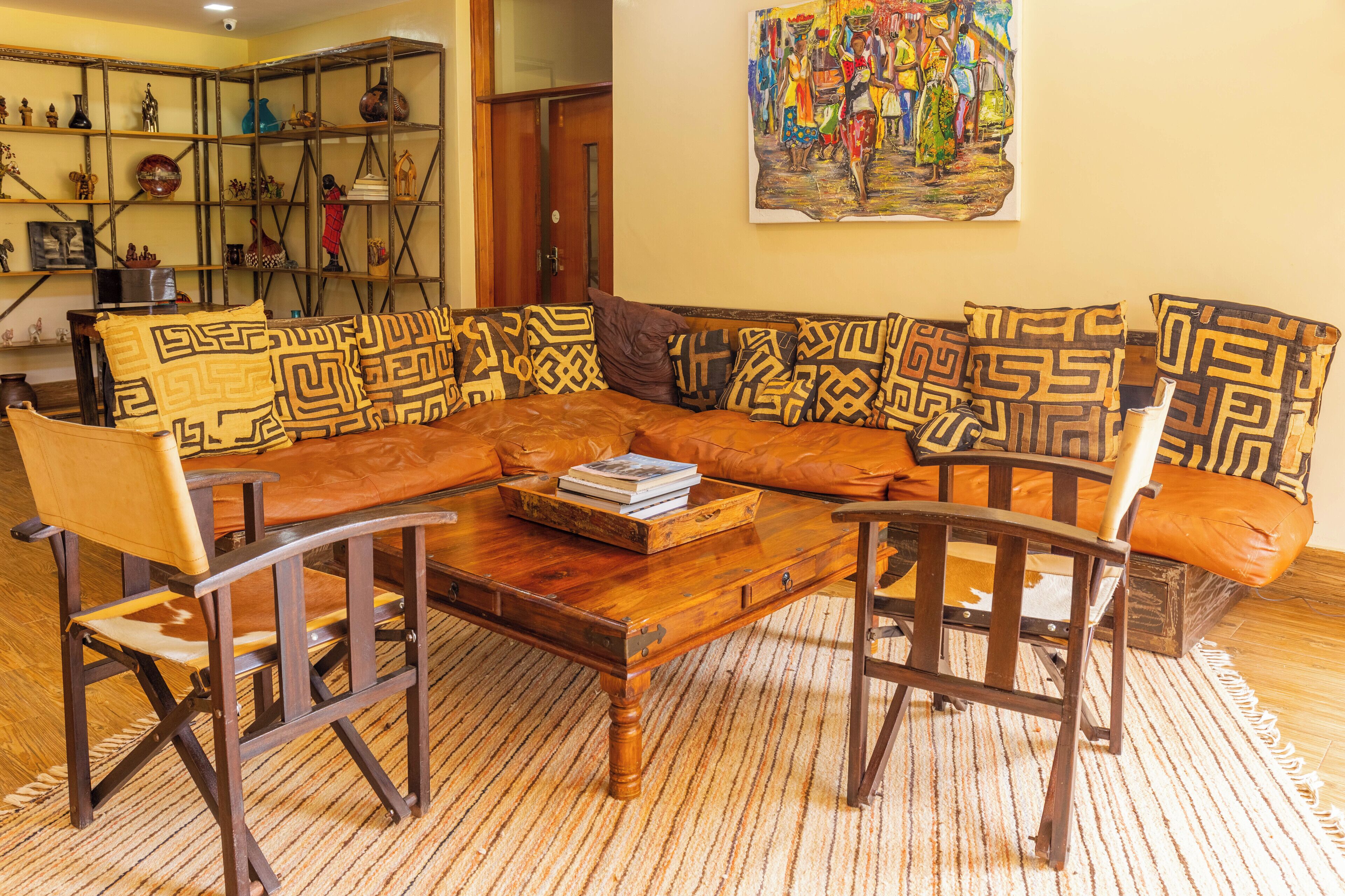 A living room with a brown leather sofa, patterned cushions, a wooden coffee table, and a bookshelf filled with decorative items.