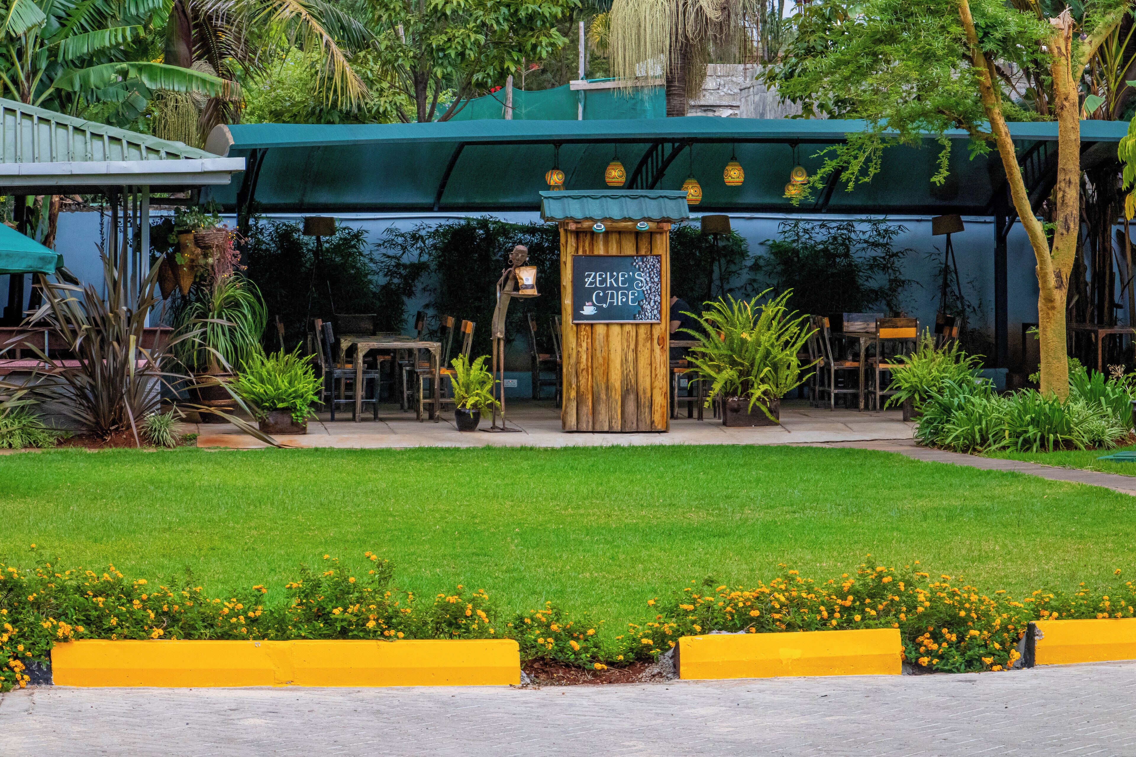 A cafe with outdoor seating, surrounded by greenery and yellow planters.