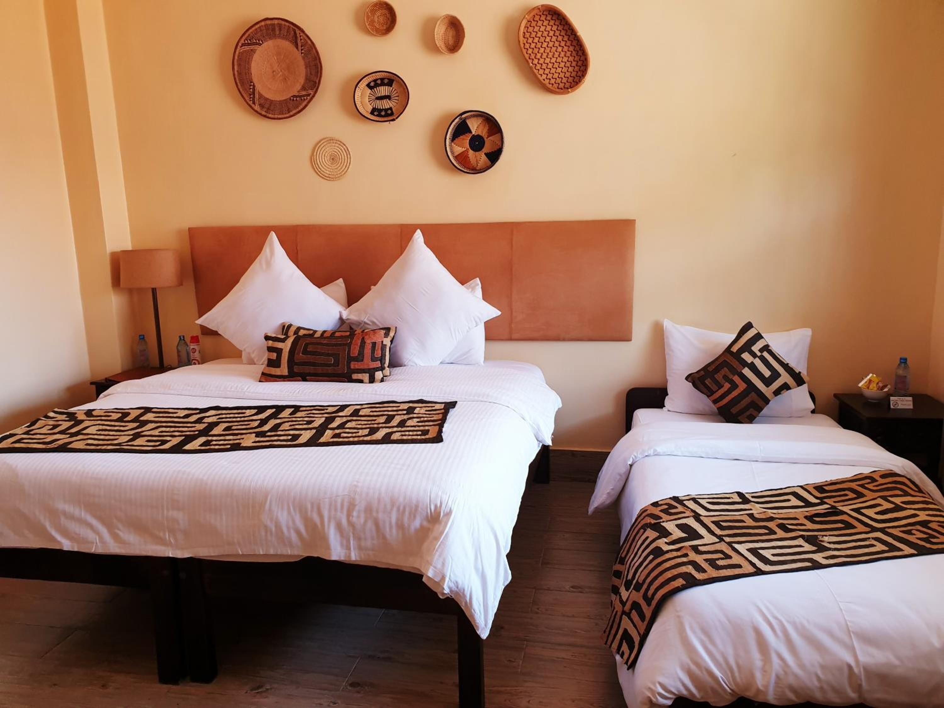 A hotel room with two beds, a headboard, and a wall decorated with woven baskets and plates.