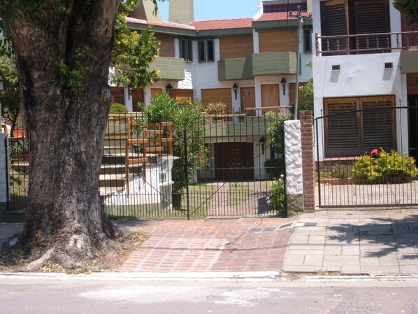 A residential building with a gated entrance, a large tree, and a paved driveway.