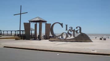 Un monumento costero con una cruz, un quiosco y una gran escultura metálica que deletrea 'La Costa'.