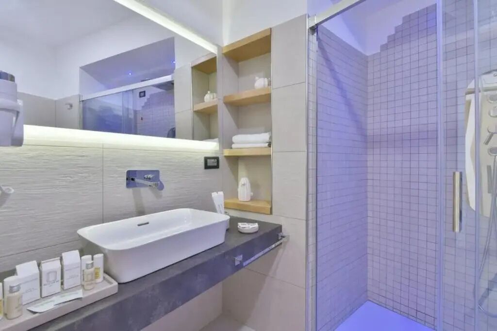 Un bagno moderno con un ampio lavandino bianco, uno specchio e un box doccia in vetro.