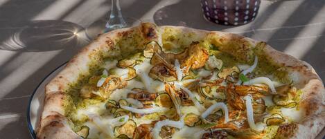 A pizza on a glass plate with a glass of white wine and a glass with a purple pattern.