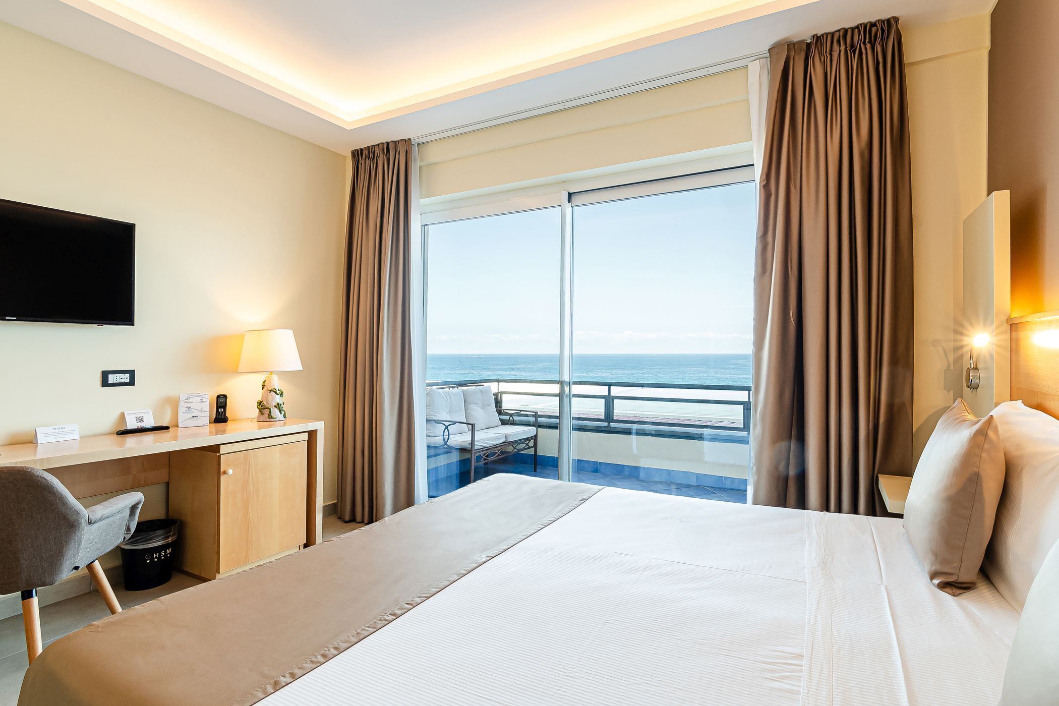 A hotel room with a bed, desk, chair, and a large window with curtains.