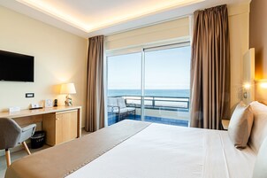 Una habitación de hotel con cama, escritorio, silla y un ventanal con cortinas.