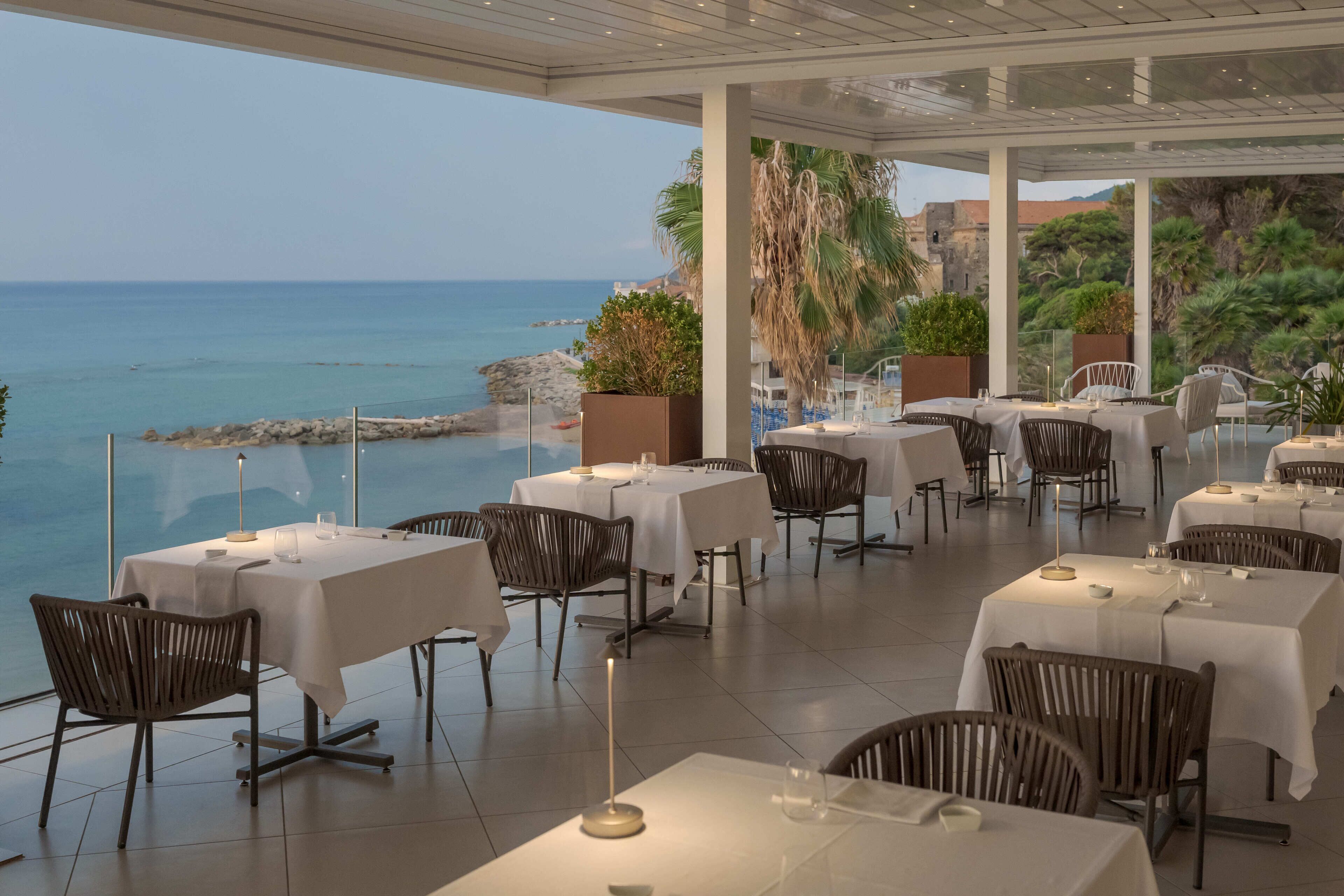 Un espace extérieur aménagé pour les repas, avec des tables et des chaises, offrant une vue sur la côte.