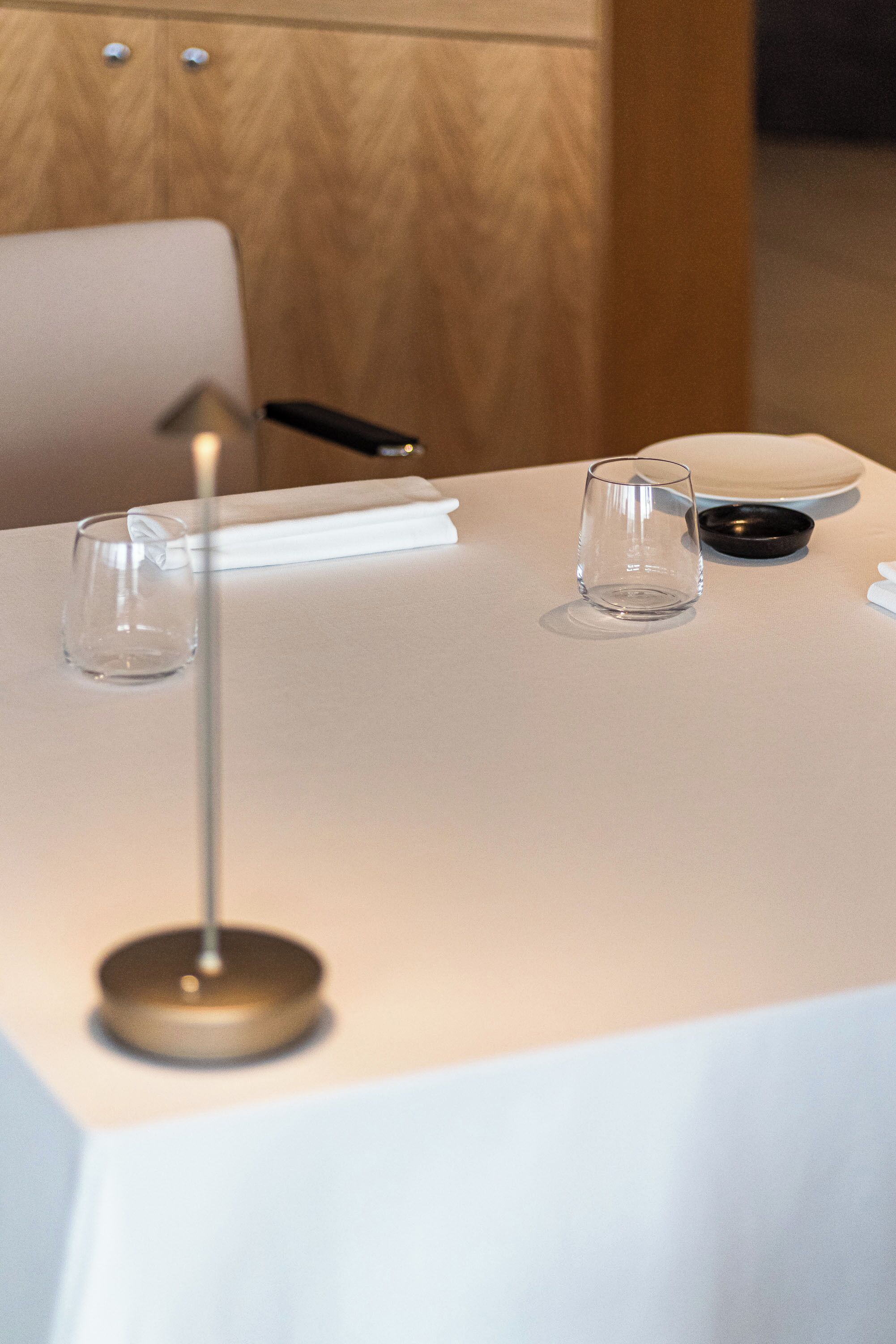 Una mesa con un vaso transparente, un posavasos negro y una servilleta blanca.