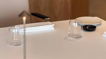 Una mesa con un vaso transparente, un posavasos negro y una servilleta blanca.