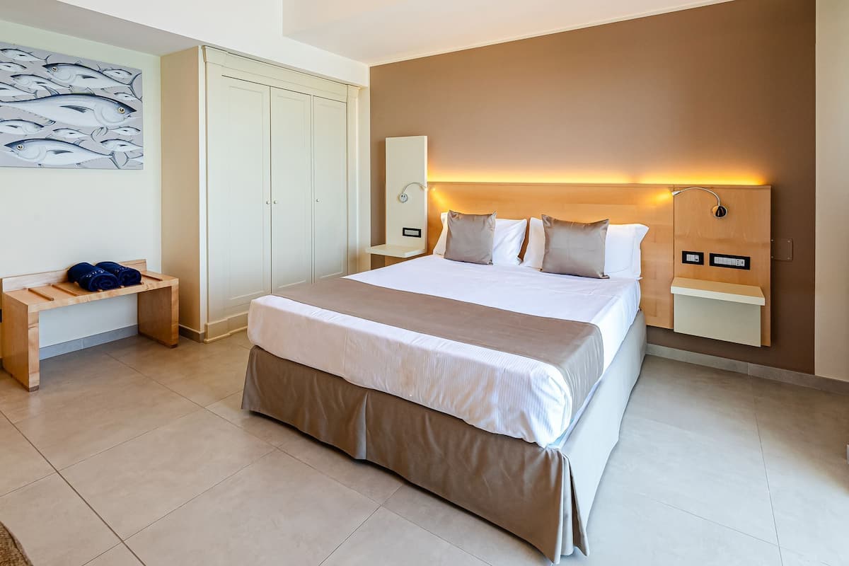 Ein Hotelzimmer mit einem großen Bett, einem Nachttisch, einem Kleiderschrank und einem an der Wand befestigten Regal.