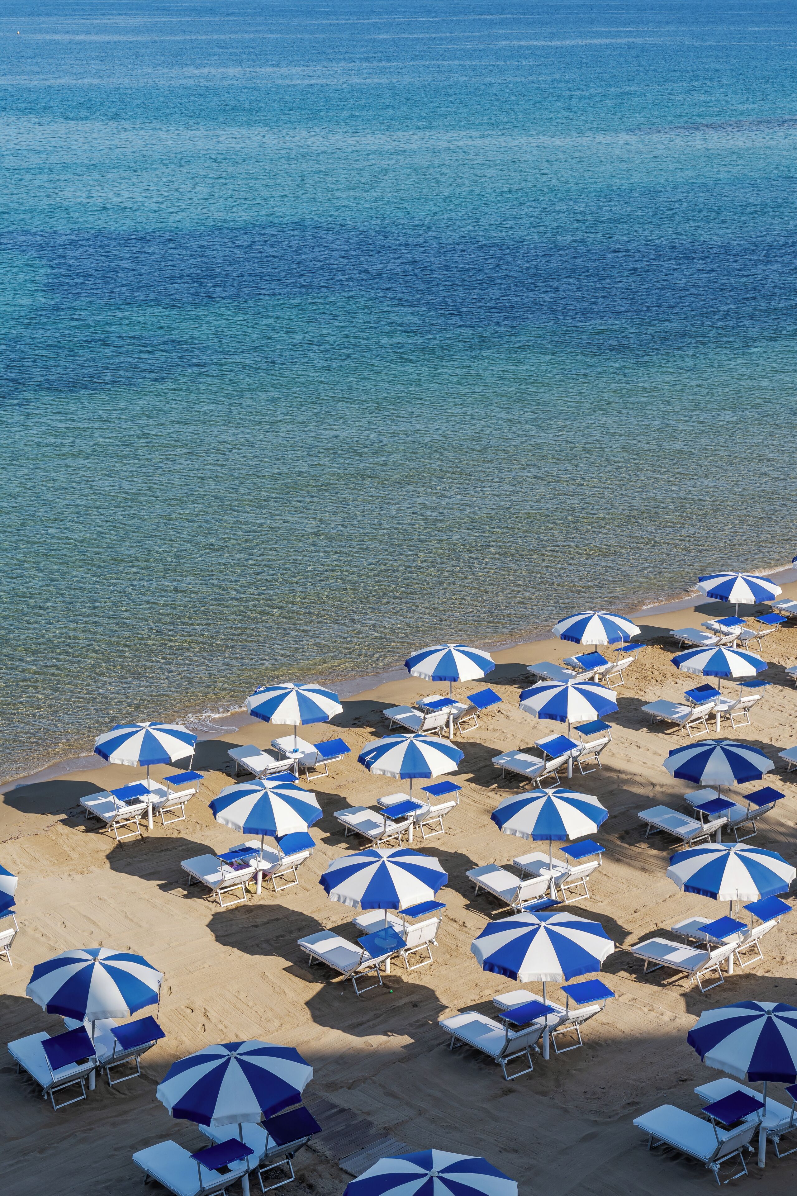 A beach with multiple rows of sunbeds and umbrellas.
