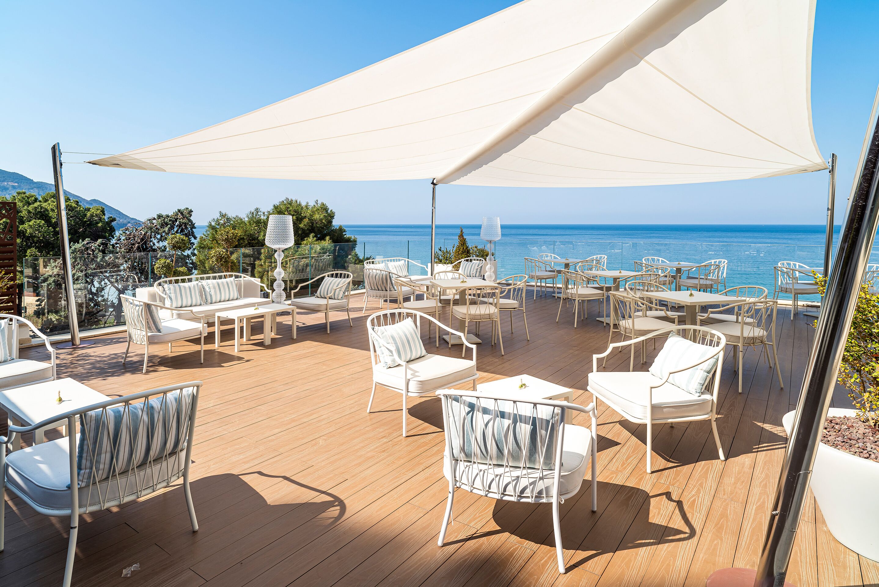 An outdoor deck with white furniture and a large canopy, overlooking a clear blue sea.