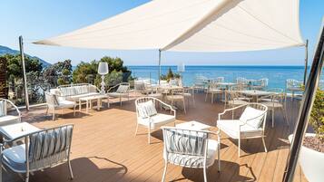 An outdoor deck with white furniture and a large canopy, overlooking a clear blue sea.
