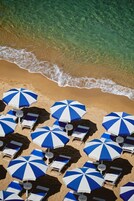 Una playa con varias sombrillas azules y blancas y sillas de playa blancas dispuestas sobre la arena.