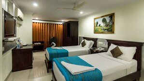 A hotel room with two beds, a desk, a chair, an air conditioning unit, a painting on the wall, and a ceiling fan. - The Central Park (Hyderabad)