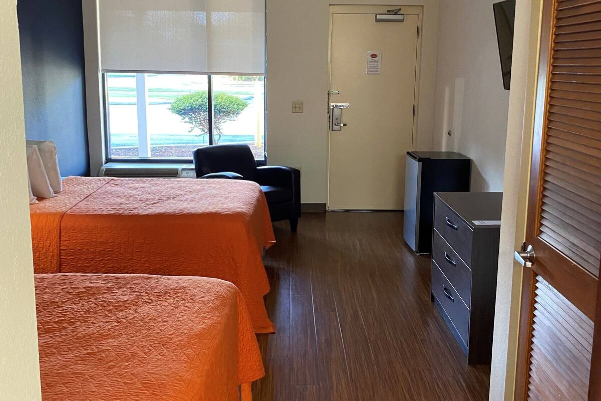 A hotel room with two beds, a desk, a chair, and a wardrobe.