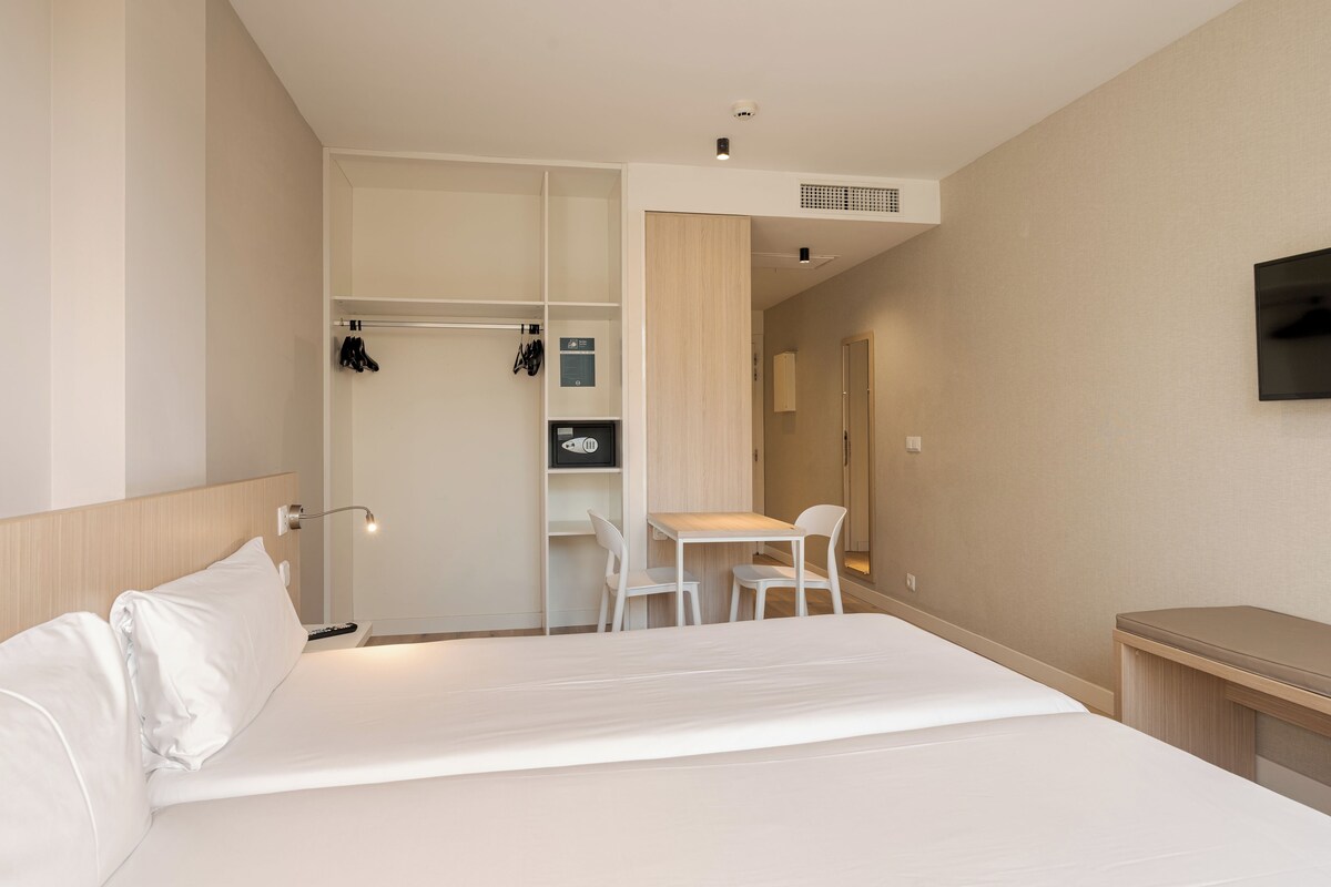 A hotel room with a bed, a desk, a chair, a wardrobe, and a television.