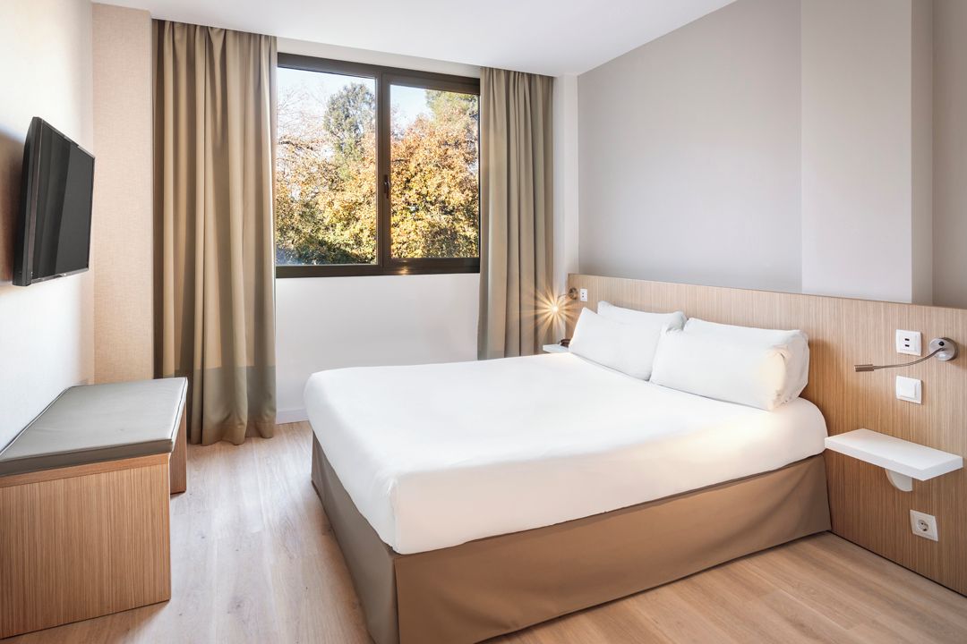 Une chambre d’hôtel avec un lit, une télévision, un bureau et une fenêtre avec des rideaux.