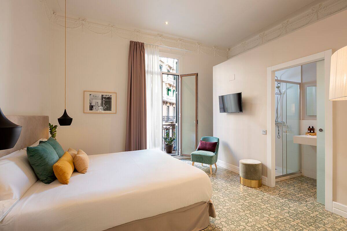 A hotel room with a bed, a chair, a TV, and a bathroom with a shower.