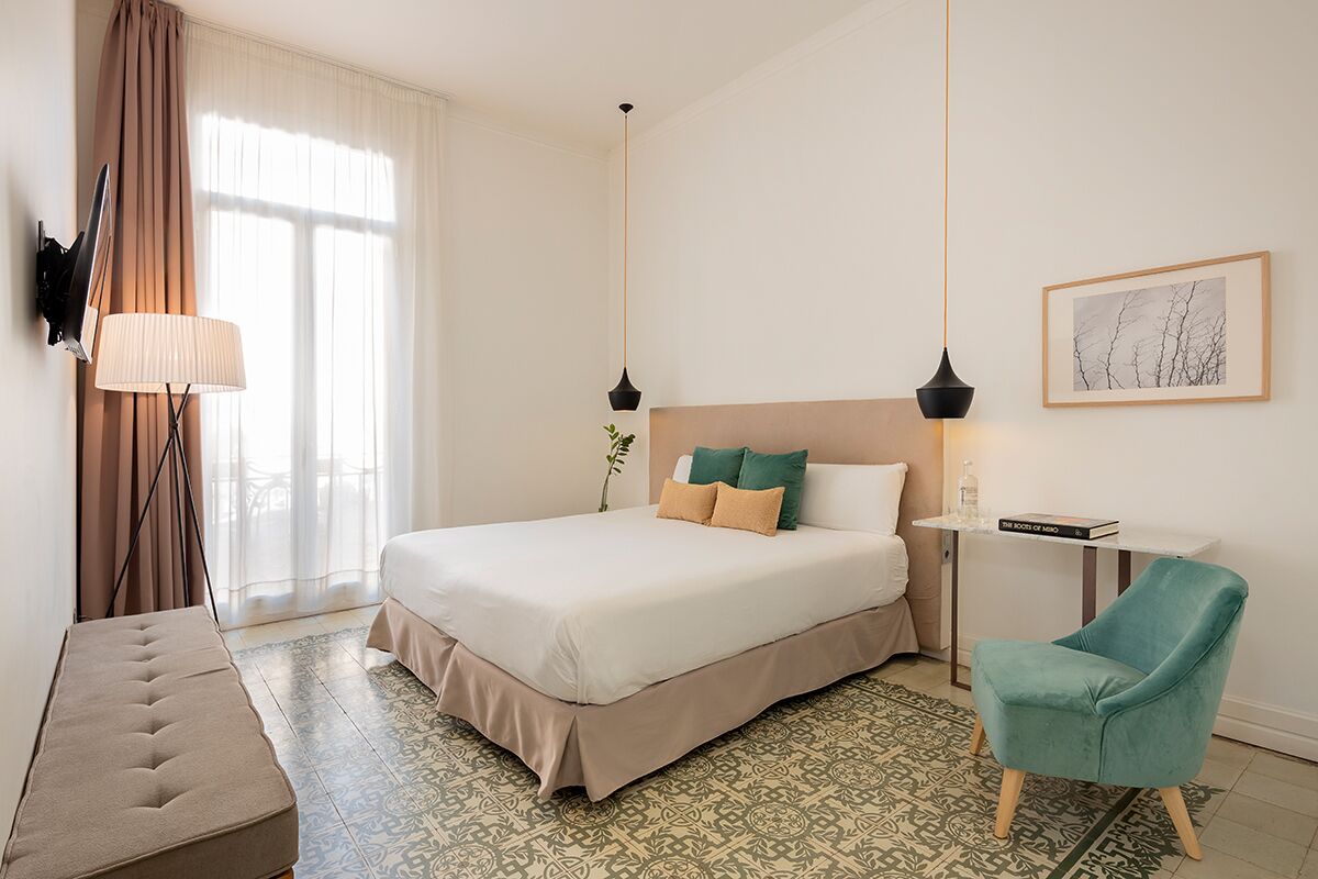 A neatly arranged hotel room with a large bed, a bedside table, a chair, a floor lamp, and a window with curtains.