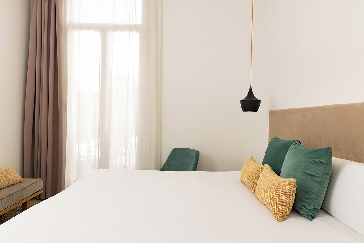 Een hotelkamer met een bed, een groene stoel, een bank en een hanglamp.